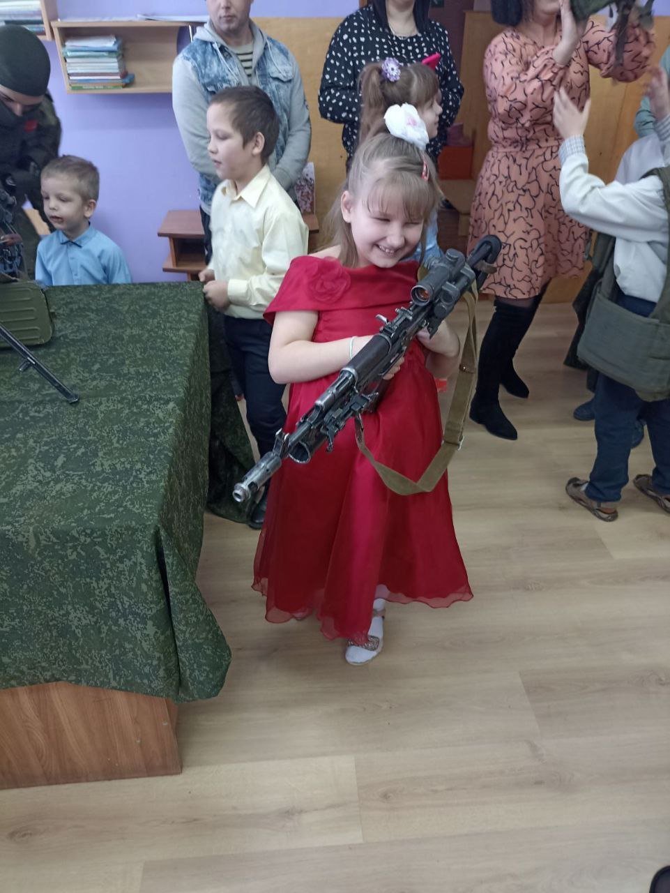 A girl from an orphanage holds a heavy rifle