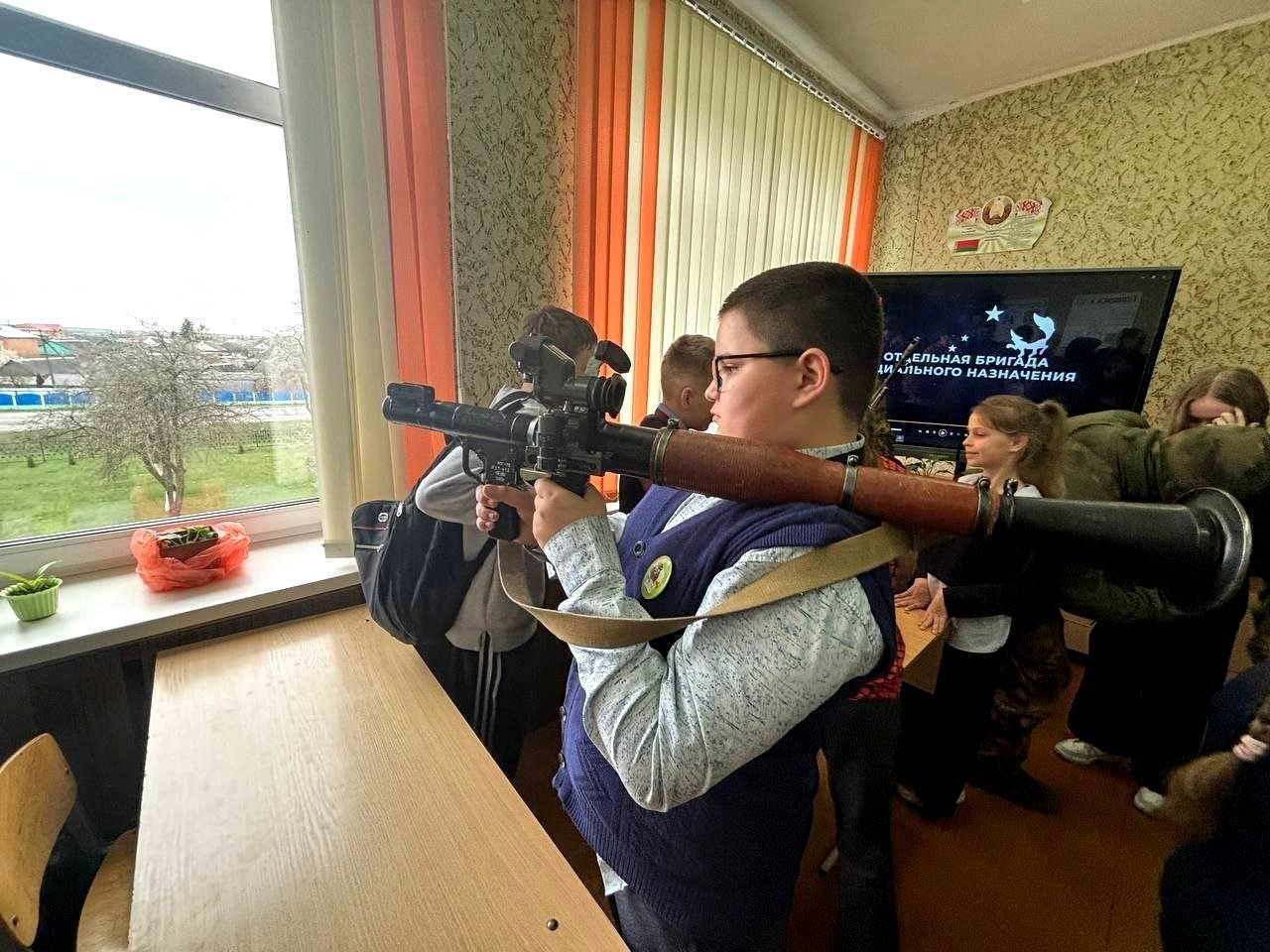 A boy aims a grenade launcher in a school classroom